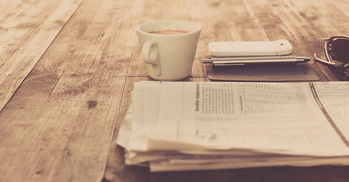 Un cadre matinal vintage chaleureux avec café, journal et smartphone sur une table en bois.